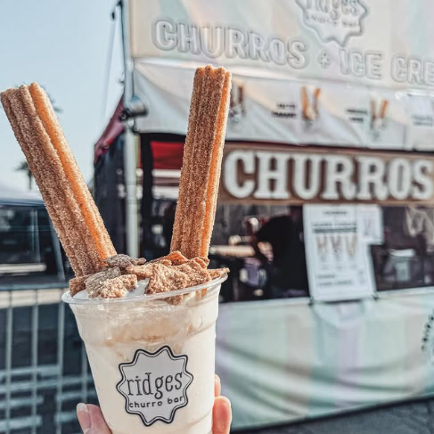 A Ridges churro sundae held in front of the truck's 'Churros + Ice Cream' banner.